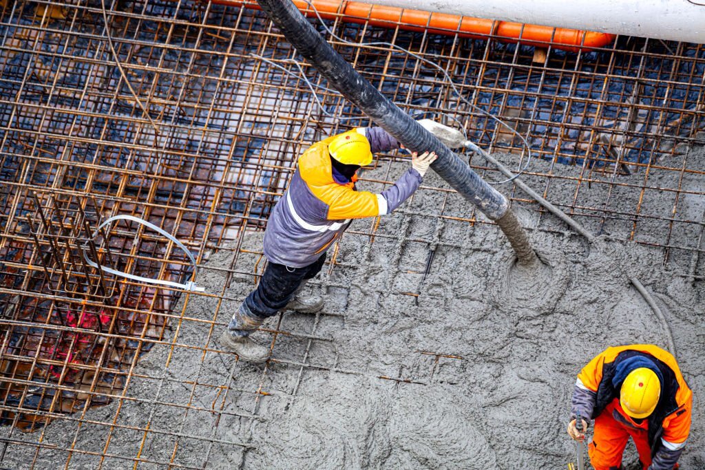 Подача бетона для прокачки жидкого раствора для заливки фундамента бетононасосом бригадой бетонщиков