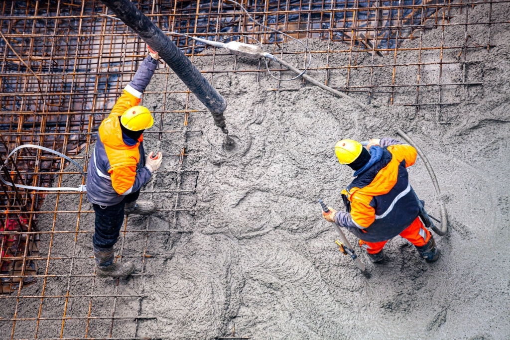 Заливка жидкого бетона бригадой бетонщиков бетононасосом в плиту фундамента здания