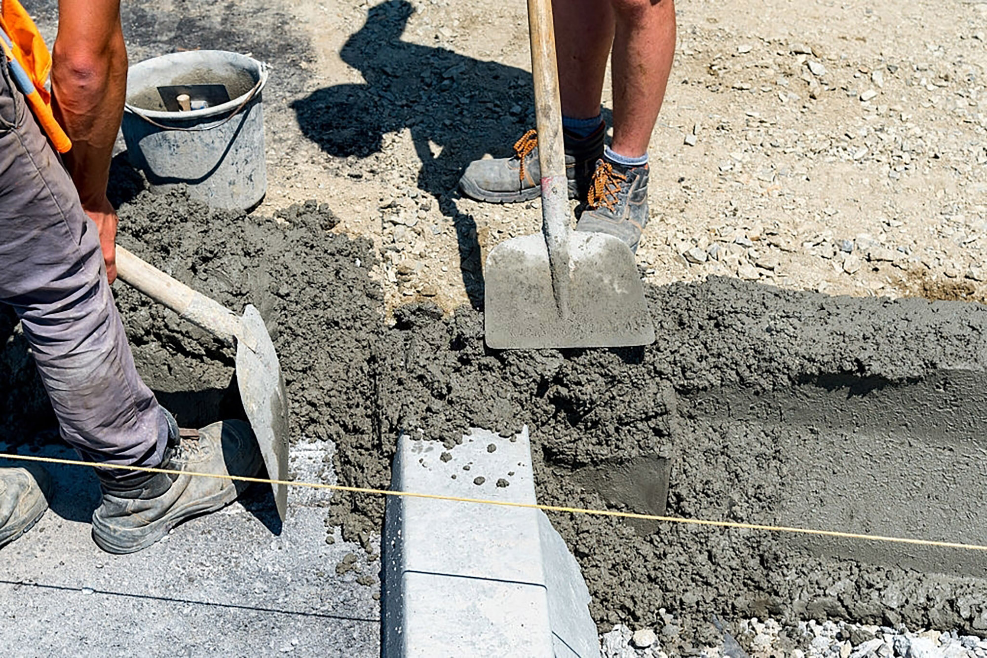 Рабочий укладывает тощий бетон лопатой